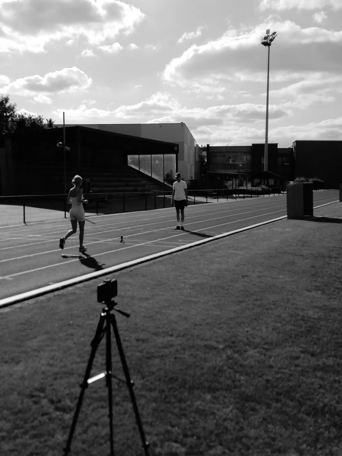 De opstelling van een loopanalyse: camera op statief langs de piste, atleet aan het lopen en de coach die meekijkt